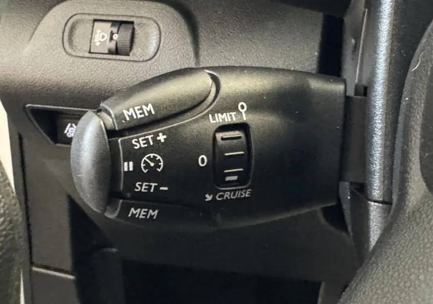 Gros plan sur la commande de régulateur de vitesse noire à gauche du volant du Citroën Berlingo blanc, intérieur.