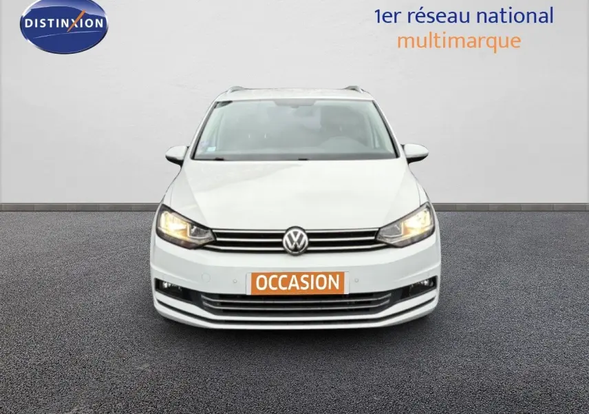 Vue avant d’un Volkswagen Touran blanc de 2018 avec phares allumés et plaque « OCCASION » visible.