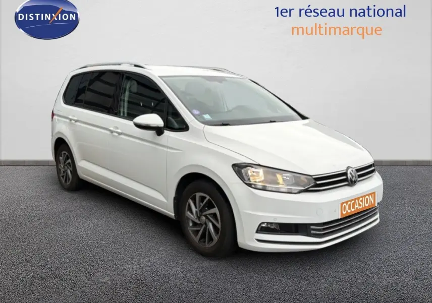 Volkswagen Touran blanc vu en 3/4 avant droit avec phares allumés et jantes bi-ton.