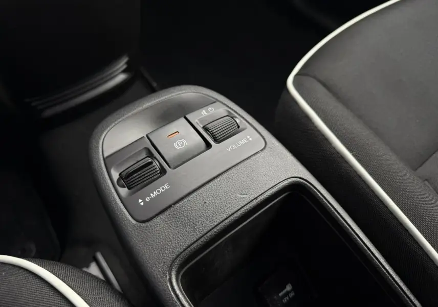 Gros plan sur la console centrale noire de la Fiat 500 électrique 2024, avec commandes e-mode et volume, sièges tissu noir.
