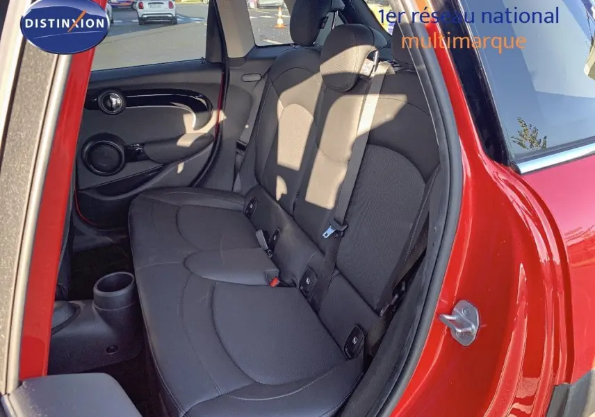 Vue côté gauche arrière sur l'intérieur d'une MINI rouge chili, mettant en valeur les sièges arrière noirs et la porte ouverte.