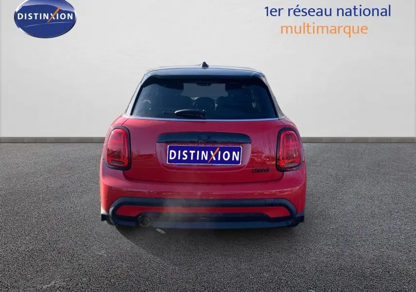 Vue arrière d'une MINI rouge chili 2023 avec toit noir et feux arrière caractéristiques allumés.