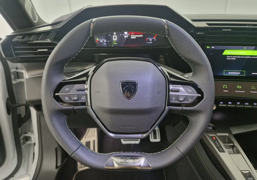 Vue rapprochée du volant cuir perforé noir avec logo Peugeot et badge GT de la 308 blanche 2025.