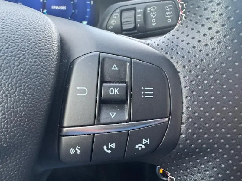 Gros plan sur les commandes multifonctions du volant perforé du Ford Puma 2023, version ST-Line X rouge vif.