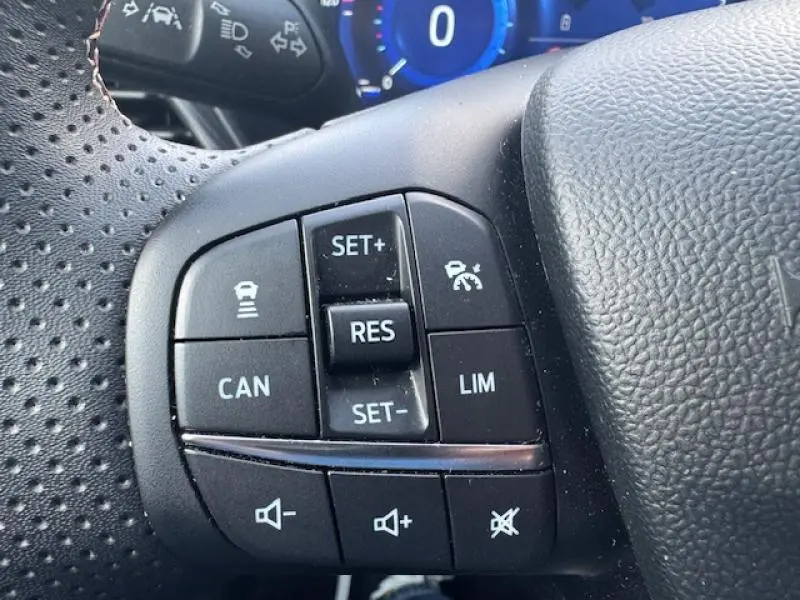 Gros plan sur les commandes de régulateur et volume au volant perforé noir du Ford Puma rouge Vivid Ruby Edition 2023.