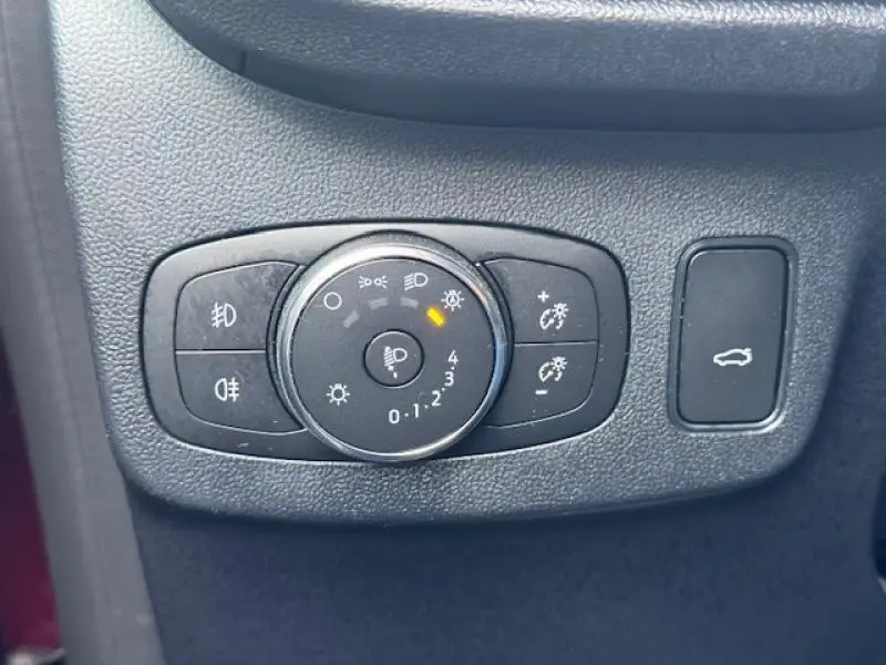 Gros plan sur les commandes d'éclairage et ouverture de coffre d'une Ford Puma rouge, intérieur noir texturé.