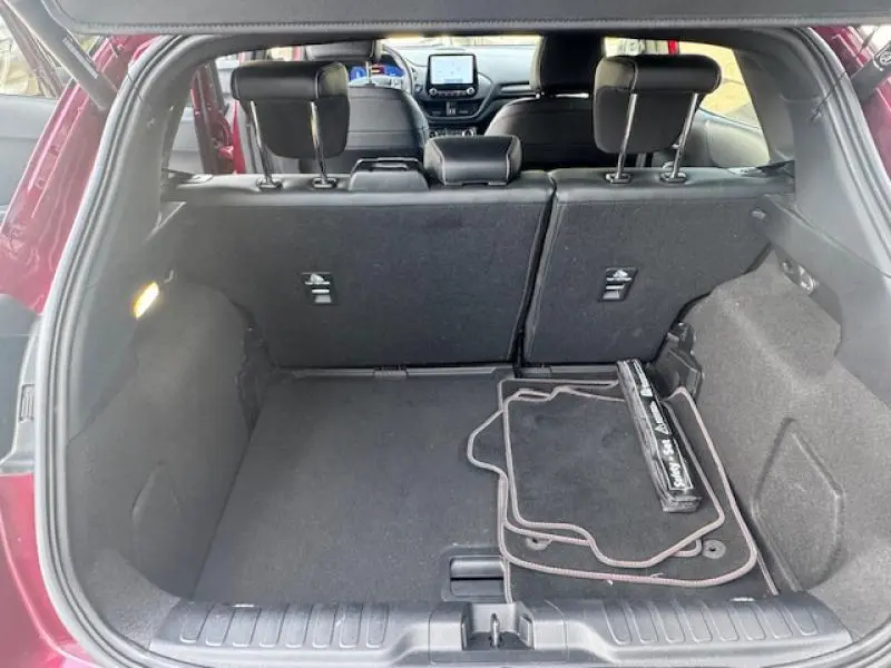 Coffre ouvert vu de l'arrière d'un Ford Puma rouge, banquette arrière relevée et tapis de sol à l'intérieur.