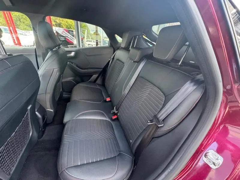 Vue intérieure côté droit sur la banquette arrière noire du Ford Puma rouge vif, avec ceinture de sécurité et appuie-têtes visibles.