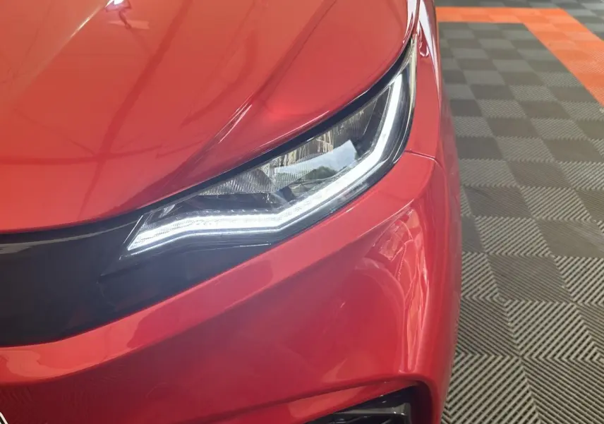 Gros plan sur le phare avant gauche d'une Aixam Ambition 0.5 City Sport rouge avec éclairage LED distinctif.