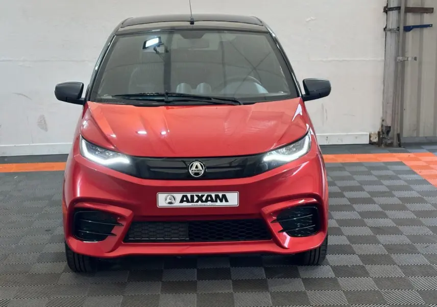 Vue de face d'une Aixam Ambition 0.5 City Sport rouge avec phares allumés et calandre noire brillante.
