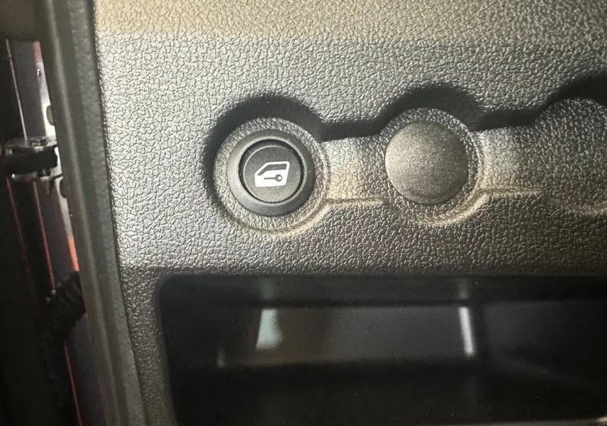 Gros plan sur le bouton d'ouverture du coffre dans l'habitacle noir de l'AIXAM AMBITION 0.5 CITY SPORT rouge.