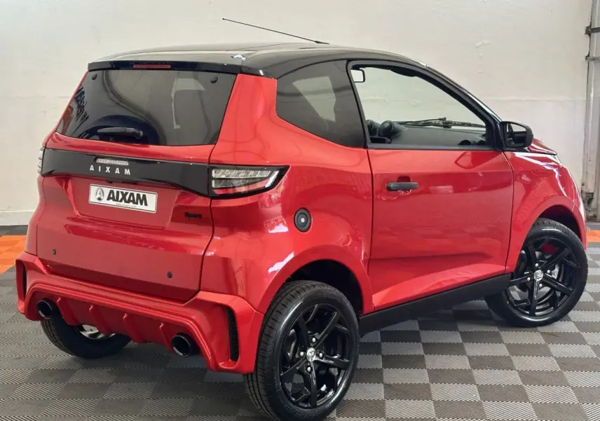 Vue 3/4 arrière droite d'une Aixam Ambition 0.5 City Sport rouge avec jantes noires et rétroviseur caméra côté gauche.