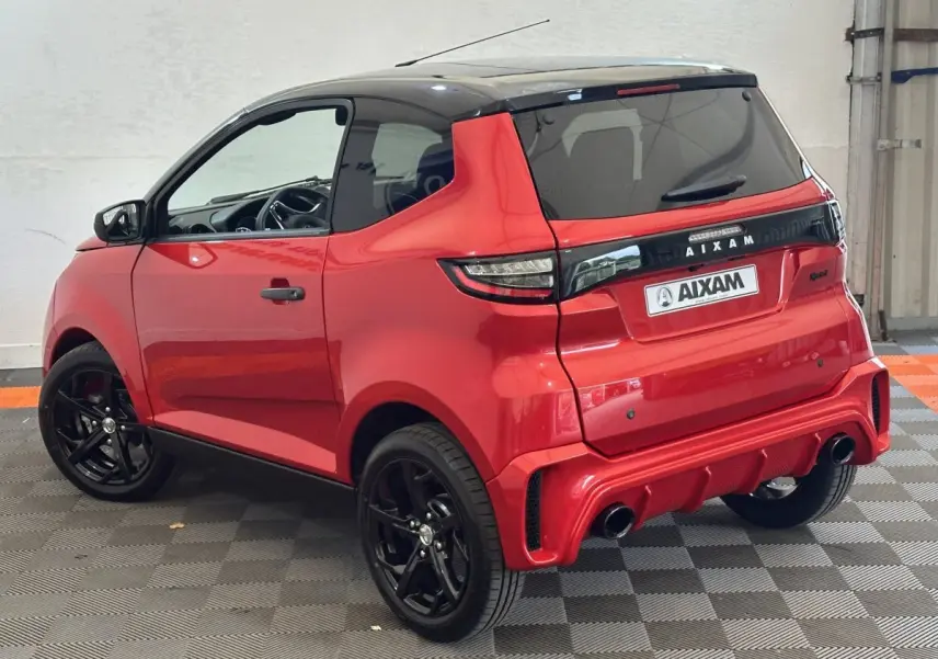 Vue 3/4 arrière droite de l'AIXAM AMBITION 0.5 CITY SPORT rouge avec toit noir et jantes noires sportives.