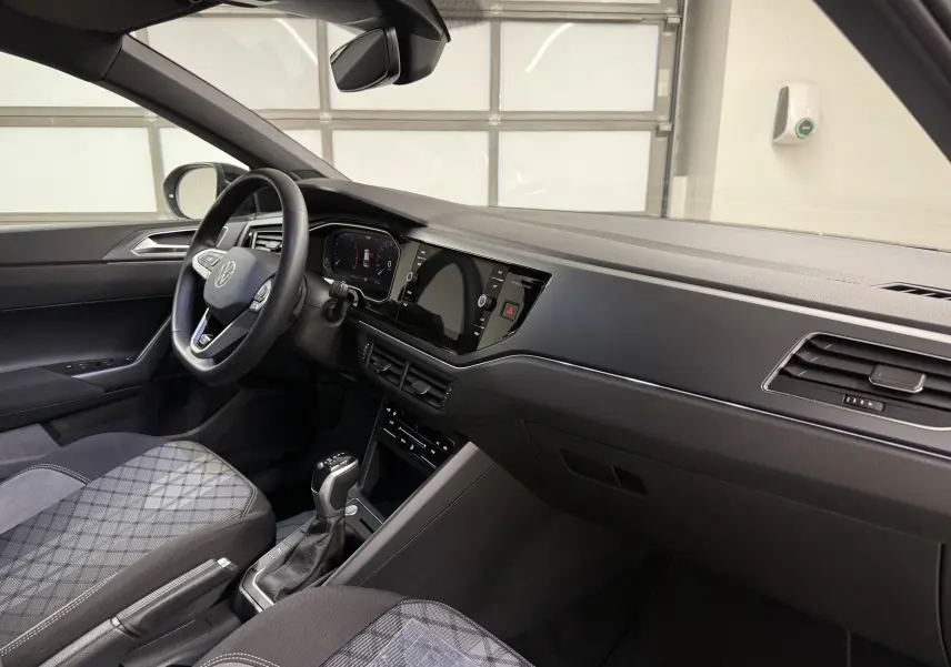 Vue intérieure côté conducteur du Volkswagen Taigo 2025, tableau de bord noir et sièges tissu à motif géométrique.