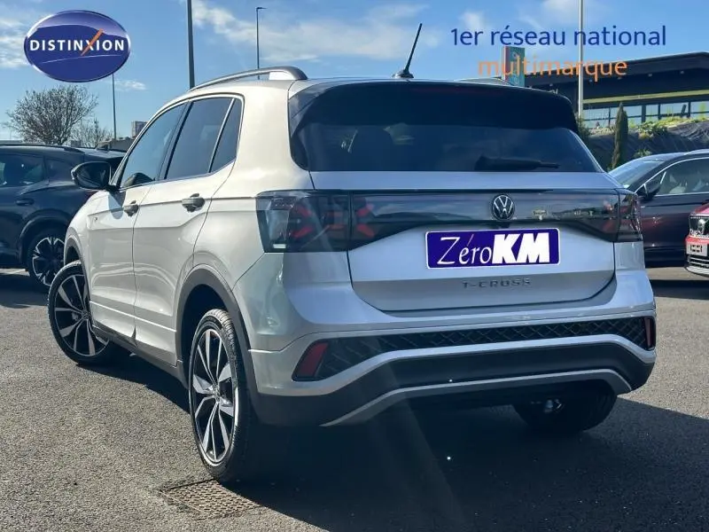 Vue 3/4 arrière droite d'un Volkswagen T-Cross argenté 2026 finition R-Line avec jantes alu et barres de toit.