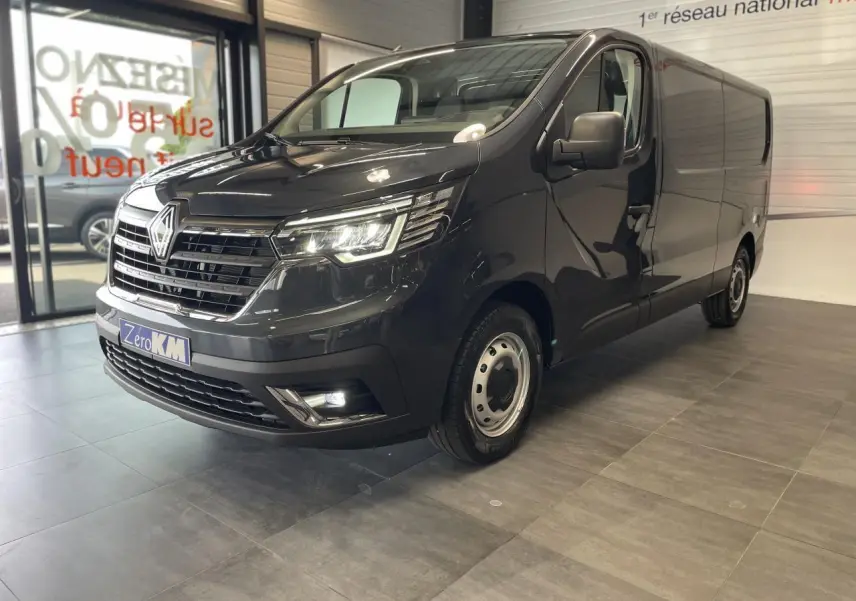 Vue 3/4 avant droit d'un Renault Trafic Fourgon gris comète avec phares LED et jantes tôles 16 pouces en showroom.