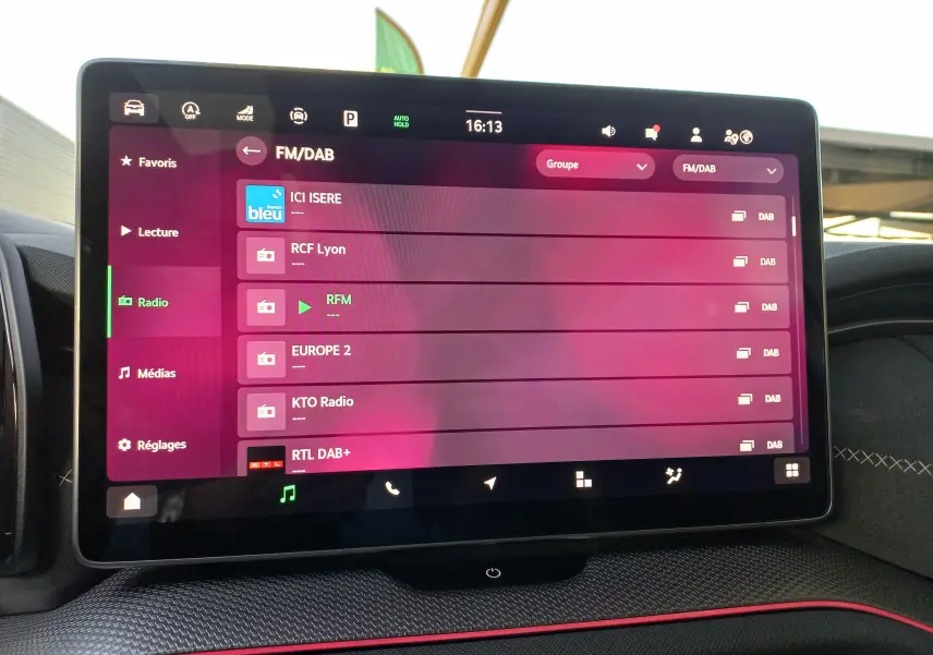 Écran tactile central du Skoda Kodiaq 2024 affichant les stations radio FM/DAB dans un intérieur avec surpiqûres blanches et bande rouge.