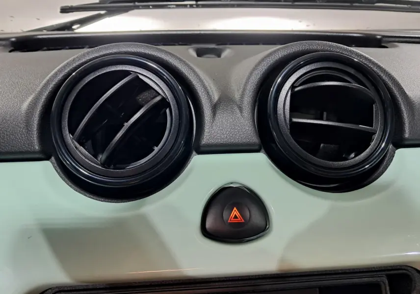 Détail du tableau de bord vert de l'AIXAM MINAUTO E chic 2026 avec deux aérateurs ronds et bouton de warning central.