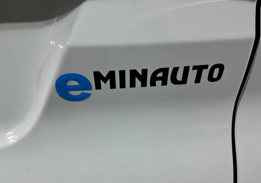 Détail du logo eMINAUTO en bleu et noir sur la carrosserie blanche d'un véhicule Aixam MINAUTO E chic 2026.