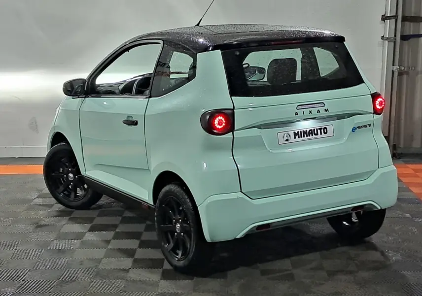 Vue 3/4 arrière droite de l'AIXAM MINAUTO E chic 2026 vert clair avec toit noir et feux arrière allumés.