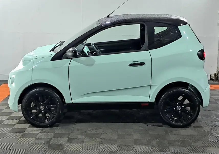 Vue de profil côté gauche d'une Aixam Minauto E chic 2026 vert clair avec toit noir et jantes noires.