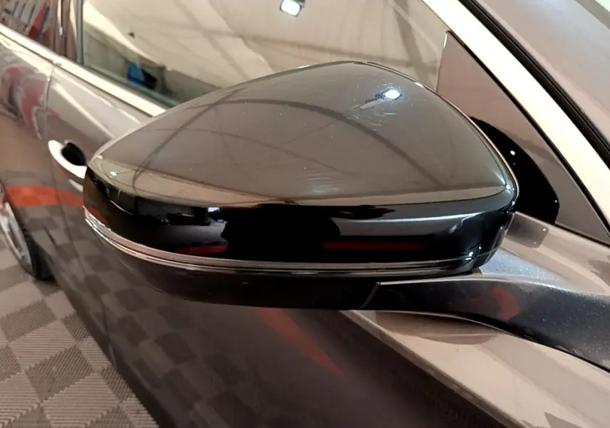 Gros plan sur le rétroviseur droit noir brillant du DS7 Crossback gris foncé, avec reflet de l'environnement intérieur.