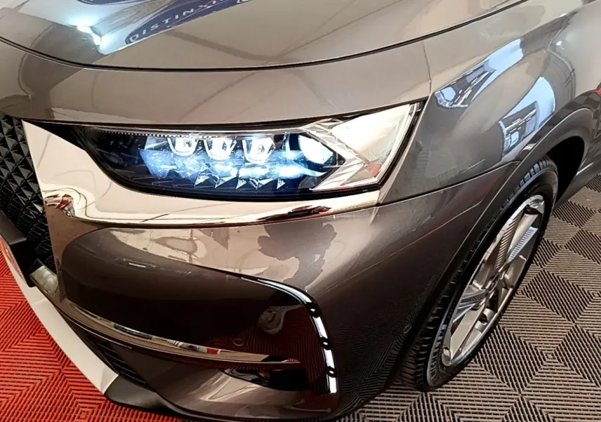 Gros plan sur le phare avant droit allumé du DS7 Crossback E-TENSE gris foncé avec détails chromés et jante visible.