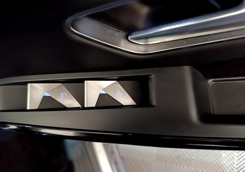Gros plan sur les commandes des vitres électriques côté conducteur du DS7 Crossback gris foncé, avec éclairage bleu.