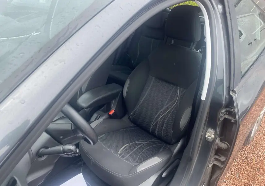 Intérieur côté conducteur d'une Peugeot 208 gris shark 2013, siège tissu avec accoudoir central visible.