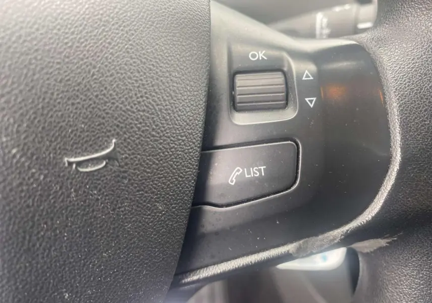 Gros plan sur les commandes multifonctions du volant noir de la Peugeot 208 gris Shark de 2013.