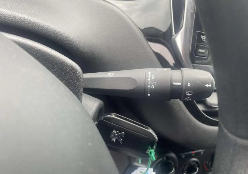 Gros plan sur la commande d’essuie-glace à gauche du volant dans l’habitacle gris foncé d’une Peugeot 208 gris shark.