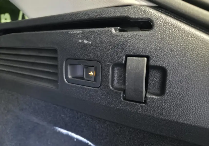 Détail du bouton d'ouverture électrique du dispositif d'attelage dans le coffre du Volkswagen Arteon blanc 2024.