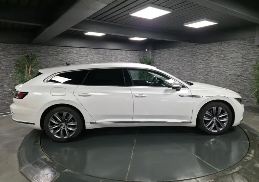 Profil côté gauche d'une Volkswagen Artéon Shooting Brake blanche nacrée avec jantes alliage 18 pouces dans un showroom.