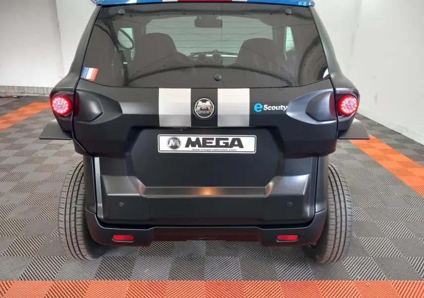 Vue arrière d'une Aixam MEGA E-Scouty Evo 2026 noire avec bandes grises et feux arrière allumés dans un garage.