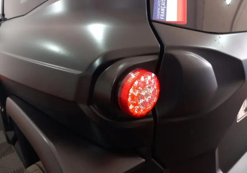 Gros plan sur le feu arrière droit rouge d’une Aixam Mega E-Scouty Evo bleu, avec autocollant "Fabrication Française".