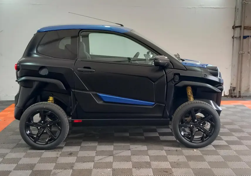 Vue de profil côté gauche d'une Aixam MEGA E-Scouty Evo 2026 bleu et noir avec suspensions jaunes et rétroviseur caméra.