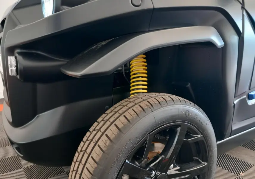 Gros plan sur l’avant droit bleu de l’AIXAM MEGA E-SCOUTY EVO 2026, mettant en valeur l’amortisseur jaune et la roue noire.