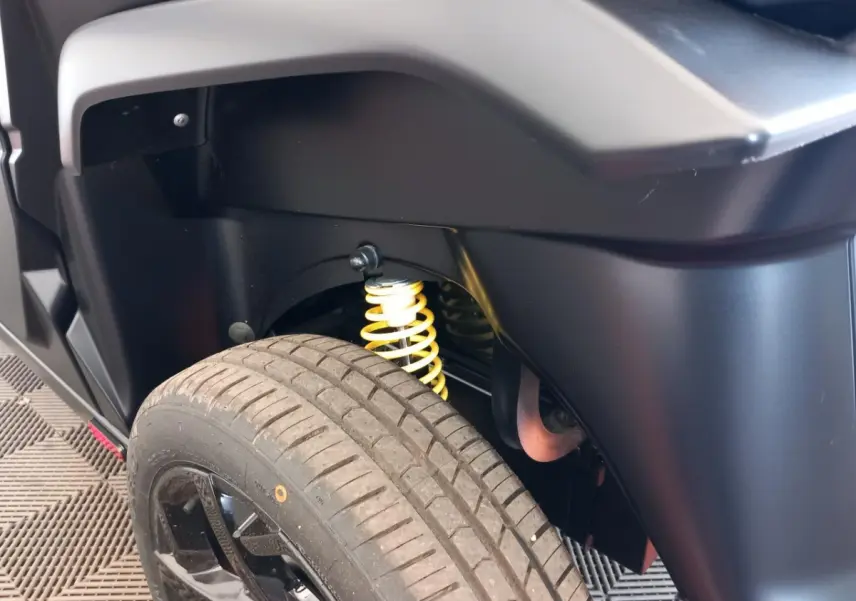 Gros plan sur la suspension arrière avec ressort jaune et roue noire du côté gauche de l'AIXAM MEGA bleu électrique.