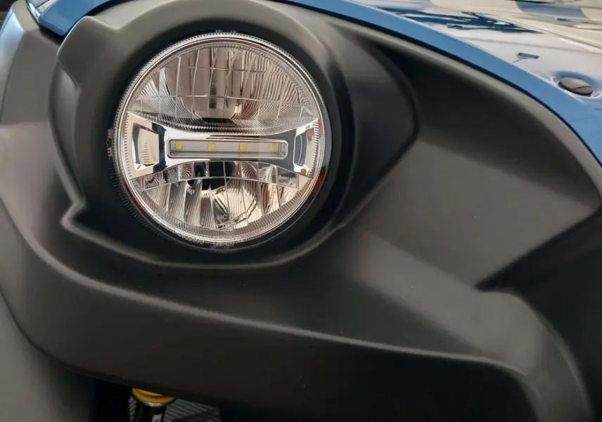 Gros plan sur le phare avant droit de l'AIXAM MEGA E-SCOUTY EVO bleu, soulignant le contour noir mat du pare-chocs.