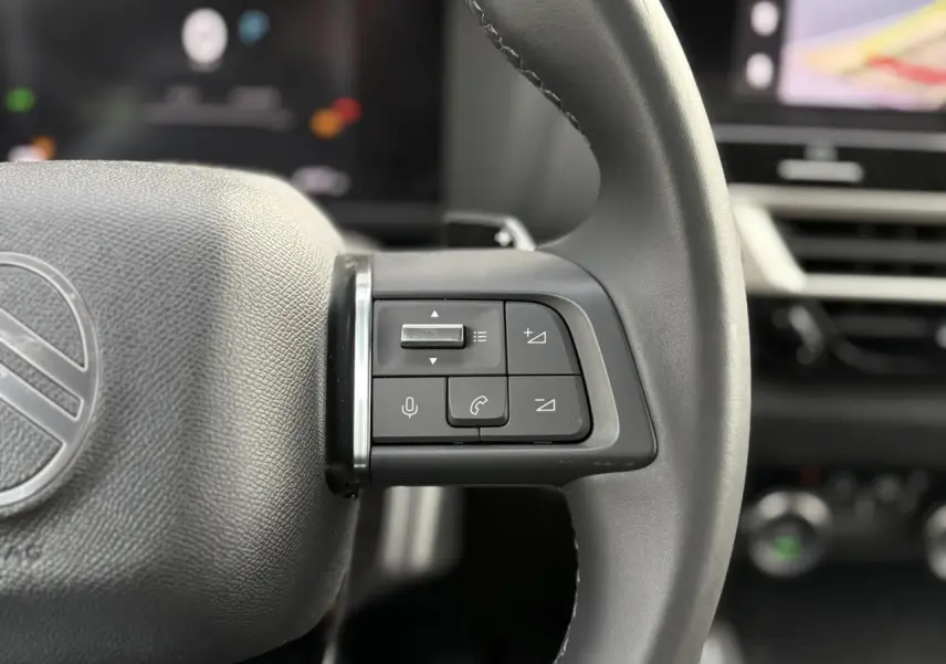 Gros plan sur les commandes du volant cuir gris de la Citroën C4 Hybrid 145 e-DSC6 Max, intérieur moderne.