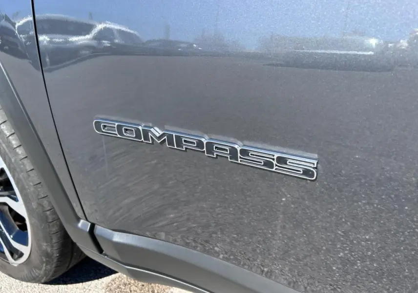 Gros plan sur l’inscription Compass côté gauche d’un Jeep Compass gris métallisé avec jante alliage visible.