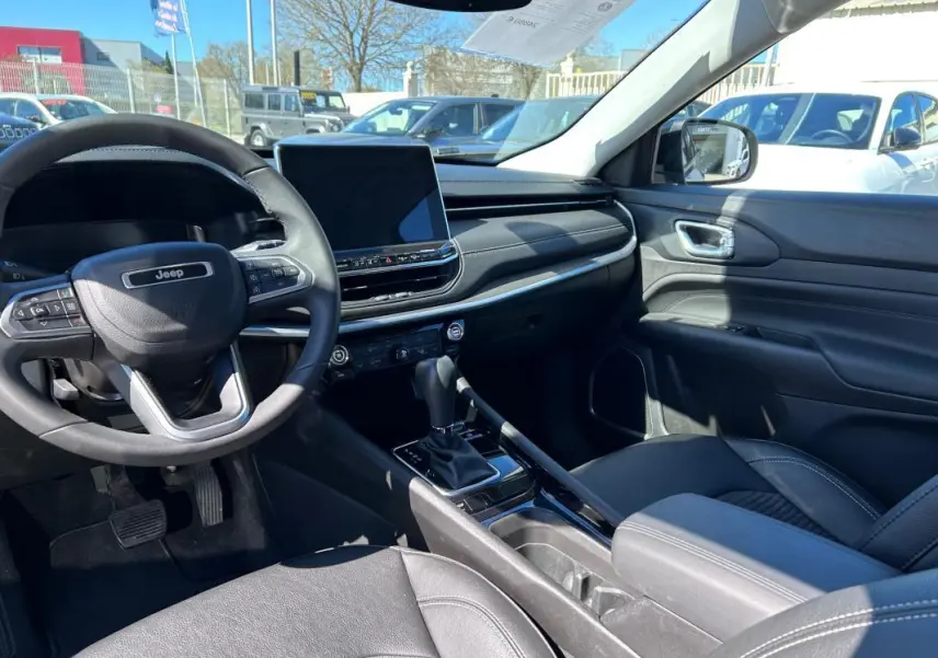 Vue intérieure côté conducteur du Jeep Compass gris 2024, avec volant multifonction, écran tactile et accoudoir central.