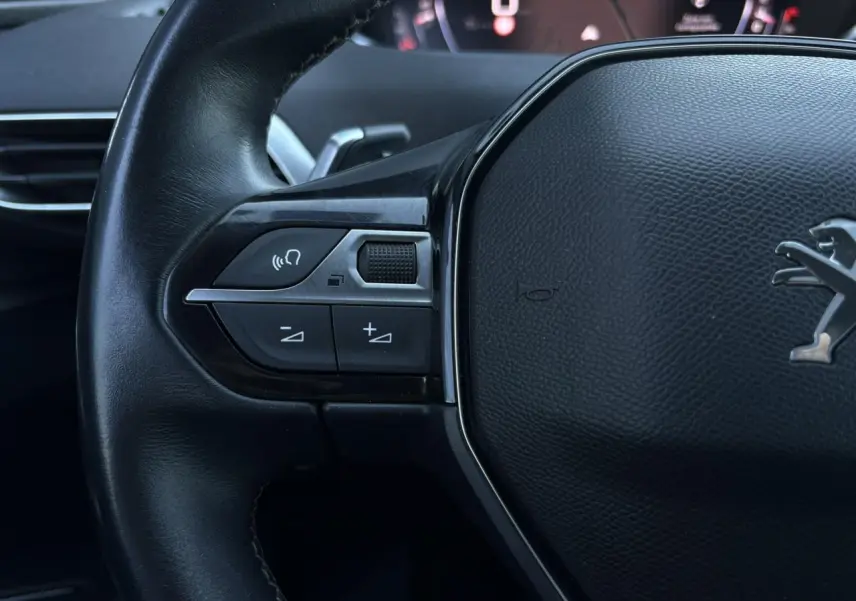 Gros plan sur le volant cuir noir du Peugeot 5008 2022 avec commandes audio et logo lion au centre.