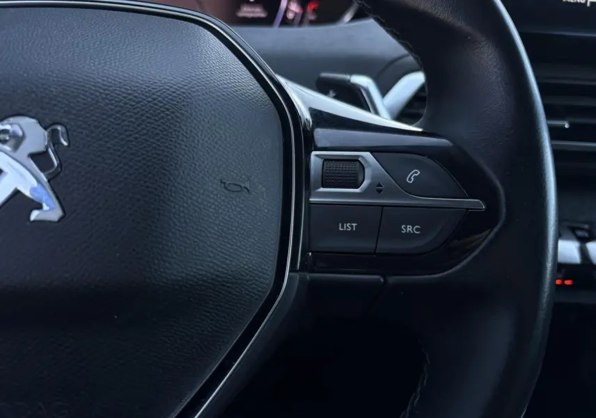 Gros plan sur le volant cuir noir du Peugeot 5008 2022 avec commandes audio et palettes au volant visibles.