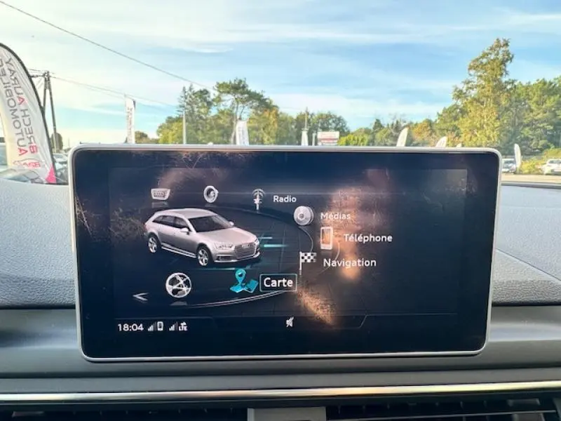 Écran central affichant le menu de navigation avec une Audi S4 Avant grise en vue 3/4 avant sur fond extérieur lumineux.
