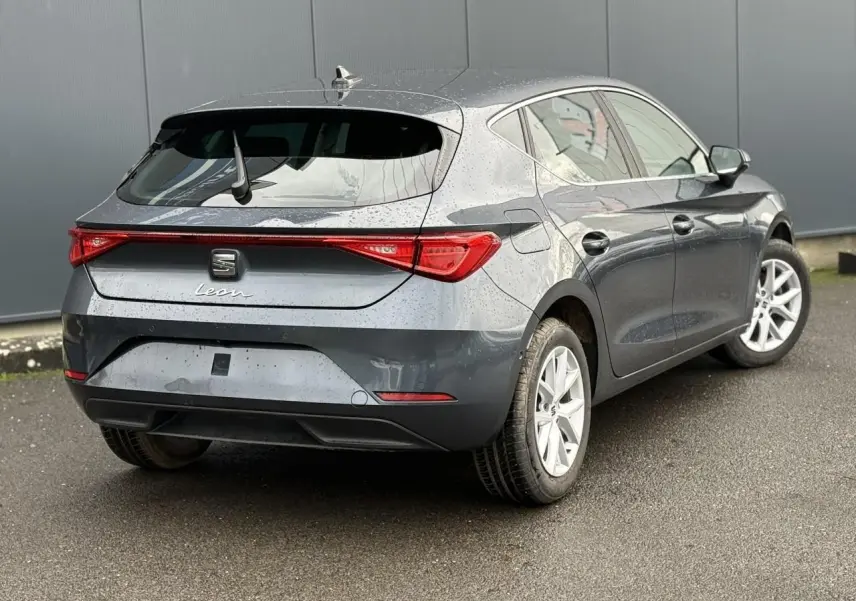 Vue 3/4 arrière droite d'une SEAT Leon 1.5 TSI 115 Style gris magnétique avec jantes alliage 16 pouces sur sol humide.