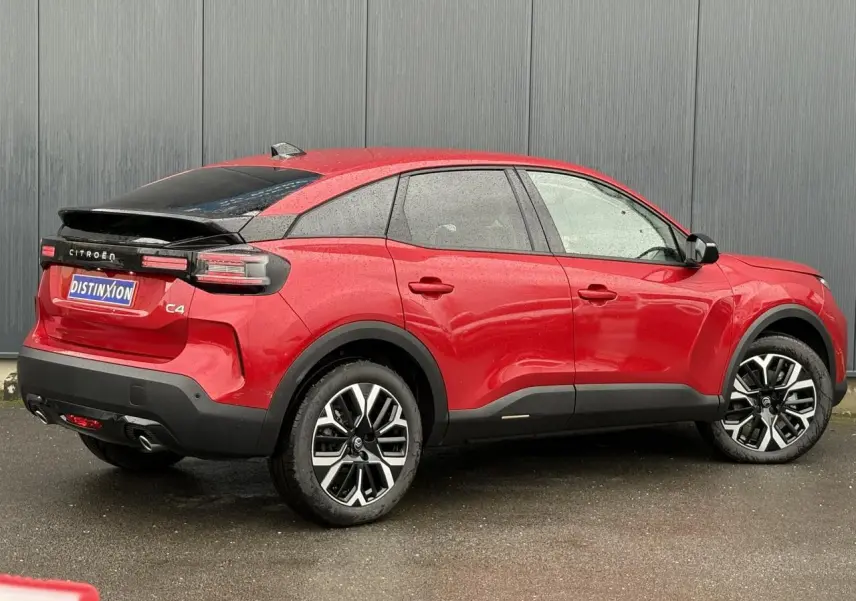 Vue 3/4 arrière droite d'une Citroën C4 Hybrid 2025 rouge Elixir avec jantes alliage et toit noir contrasté.