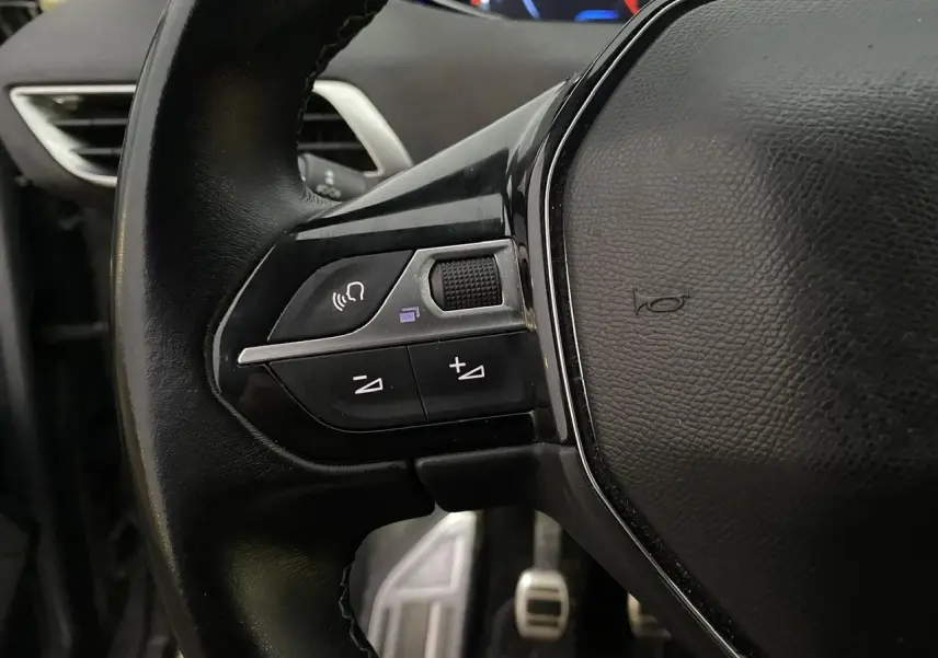 Gros plan sur les commandes au volant à gauche du Peugeot 3008 gris Artense, avec pédales visibles en arrière-plan.
