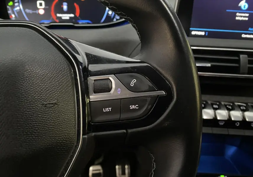 Gros plan sur les commandes au volant à droite en cuir noir du Peugeot 3008 gris Artense, avec tableau de bord et écran tactile en arrière-plan.