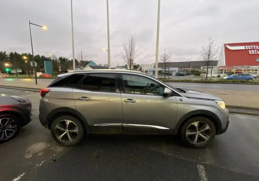 Profil côté droit du Peugeot 3008 gris Artense garé en extérieur sous un ciel nuageux.